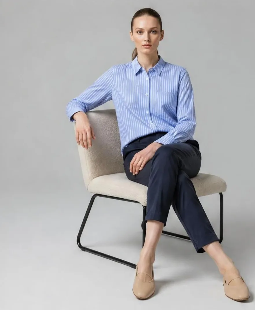 AI-generated studio photo of a model wearing a blue striped shirt and navy chinos, seated in a lounge chair