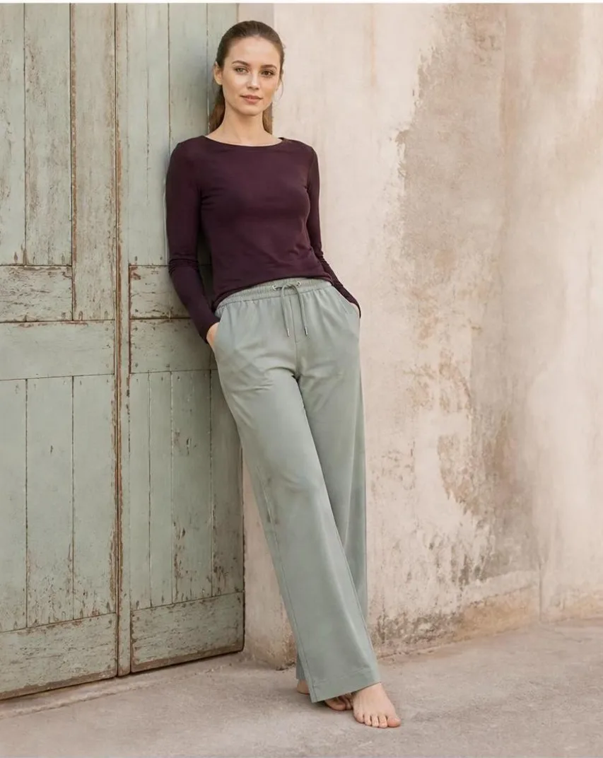 AI-generated outdoor photo of a model wearing a maroon top and sage lounge pants, leaning against a weathered rustic door