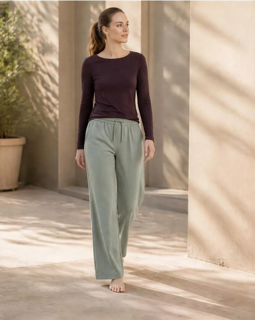 AI-generated outdoor photo of a model walking in a maroon top and sage lounge pants through a sunlit courtyard