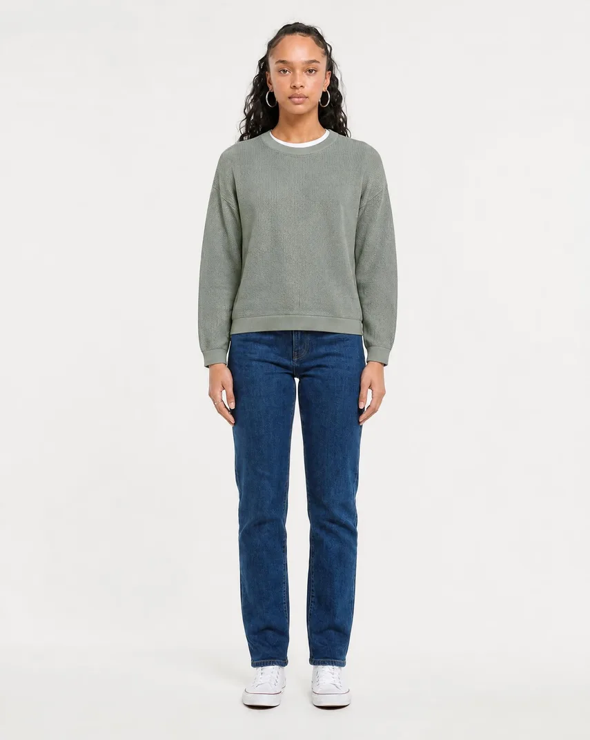 AI-generated studio photo of a model wearing a sage green knit sweater and straight-leg jeans on a clean white background