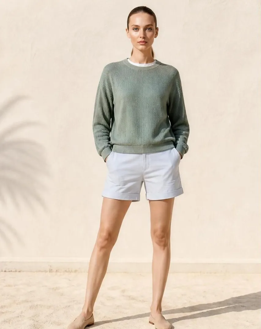 AI-generated outdoor photo of a model wearing a sage knit sweater and white shorts on a sunlit sandy terrace